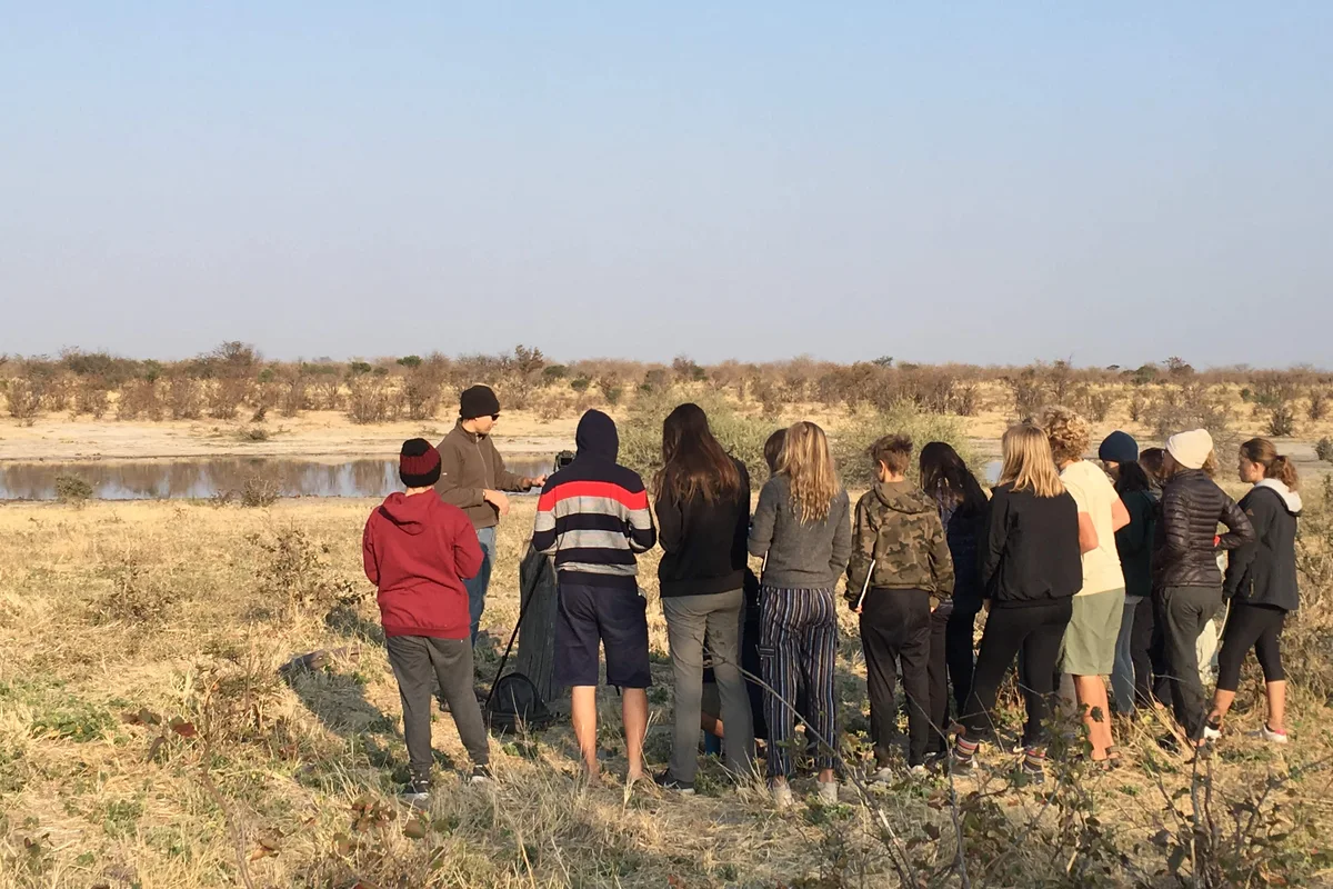 Students gather around a local guide beside a waterhole in Botswana